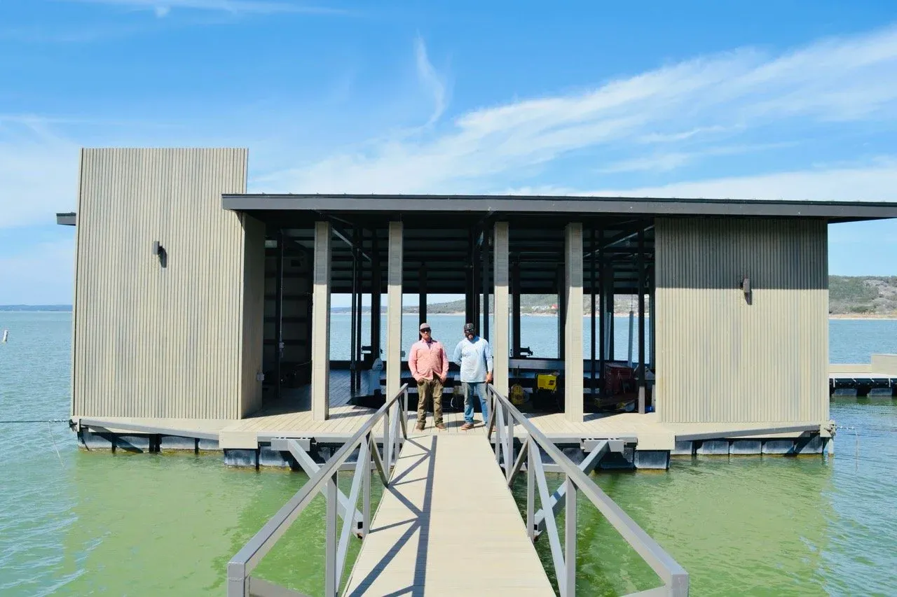 Two people standing on the gangway in front of a finished modern floating boathouse