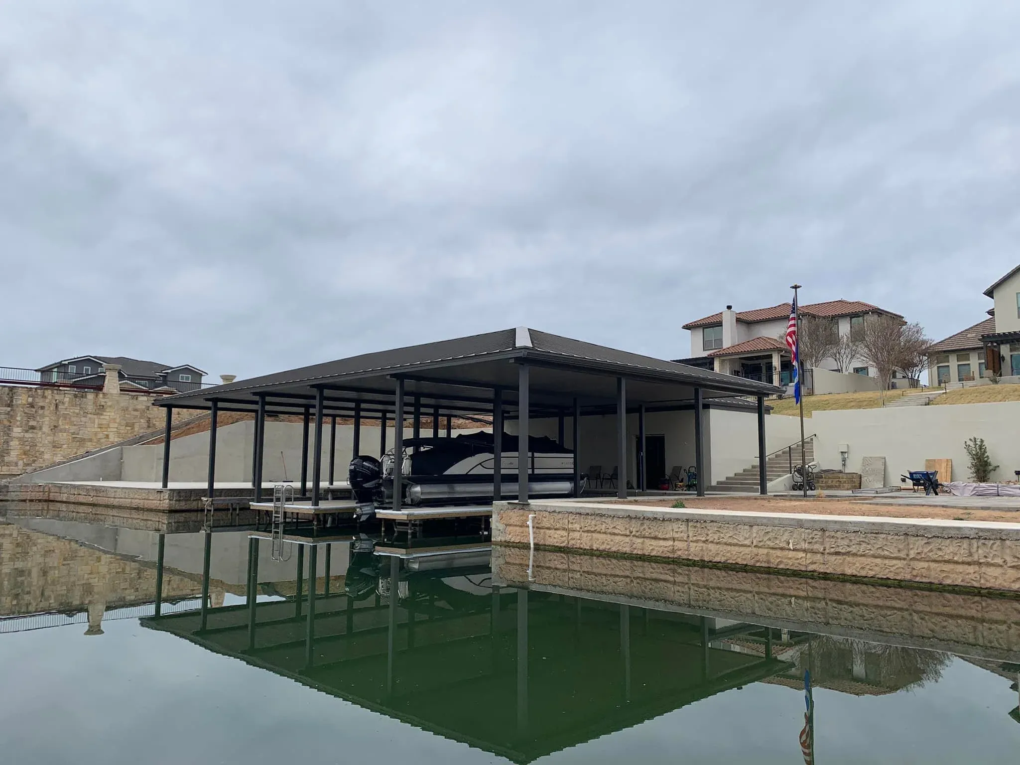 Covered stationary dock with a boat in the slip reflected in calm water
