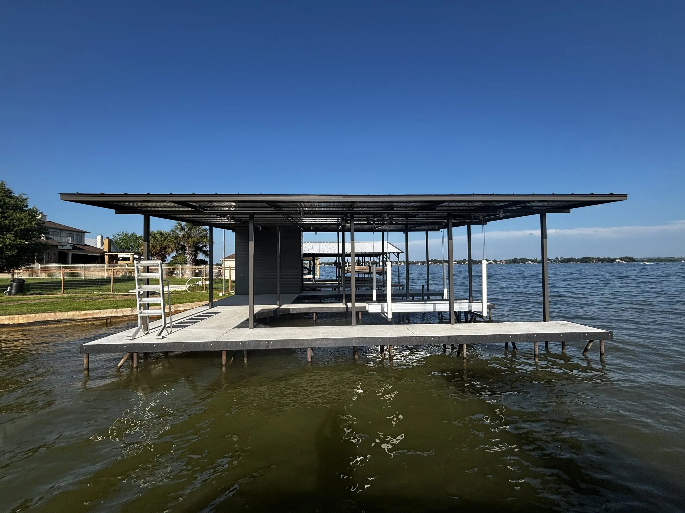Front view of the flat-roof boathouse from the water, with a ladder and open slips under the roof