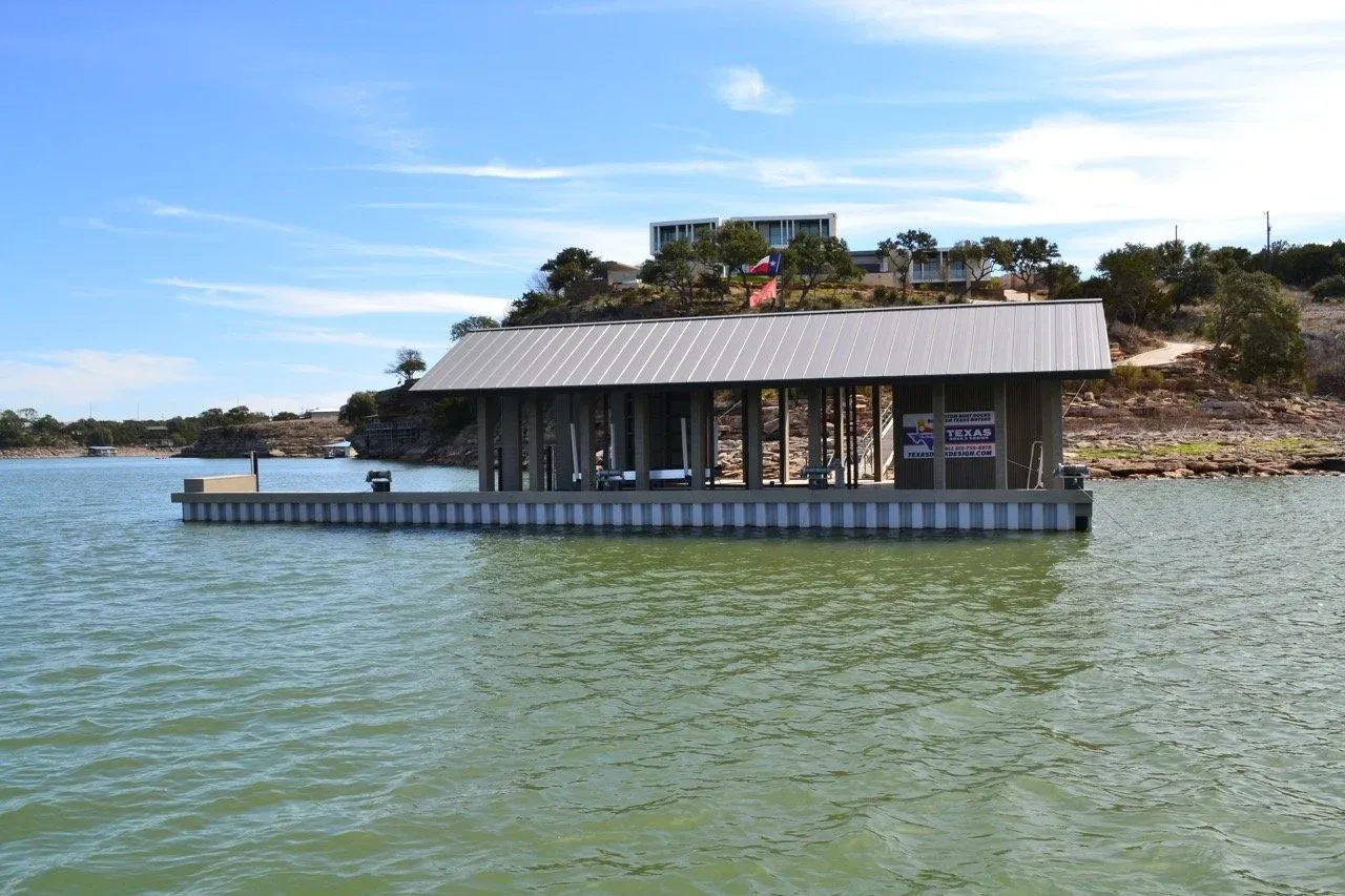 Floating boathouse with a metal roof on a Hill Country lake below a hillside home