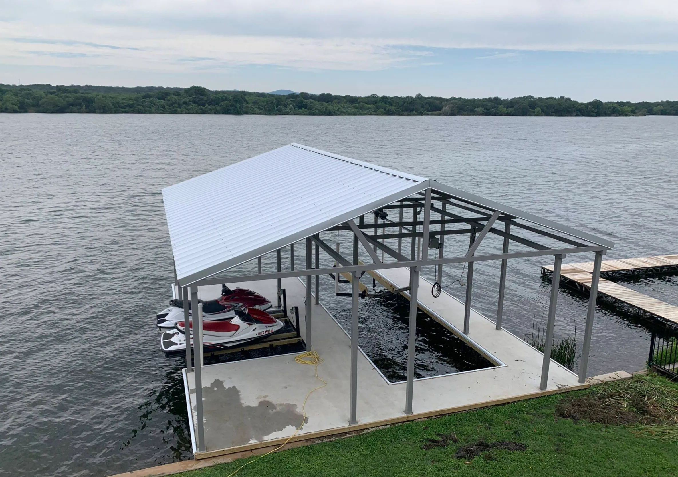 Covered dock with two jet skis on PWC lifts beside an open slip