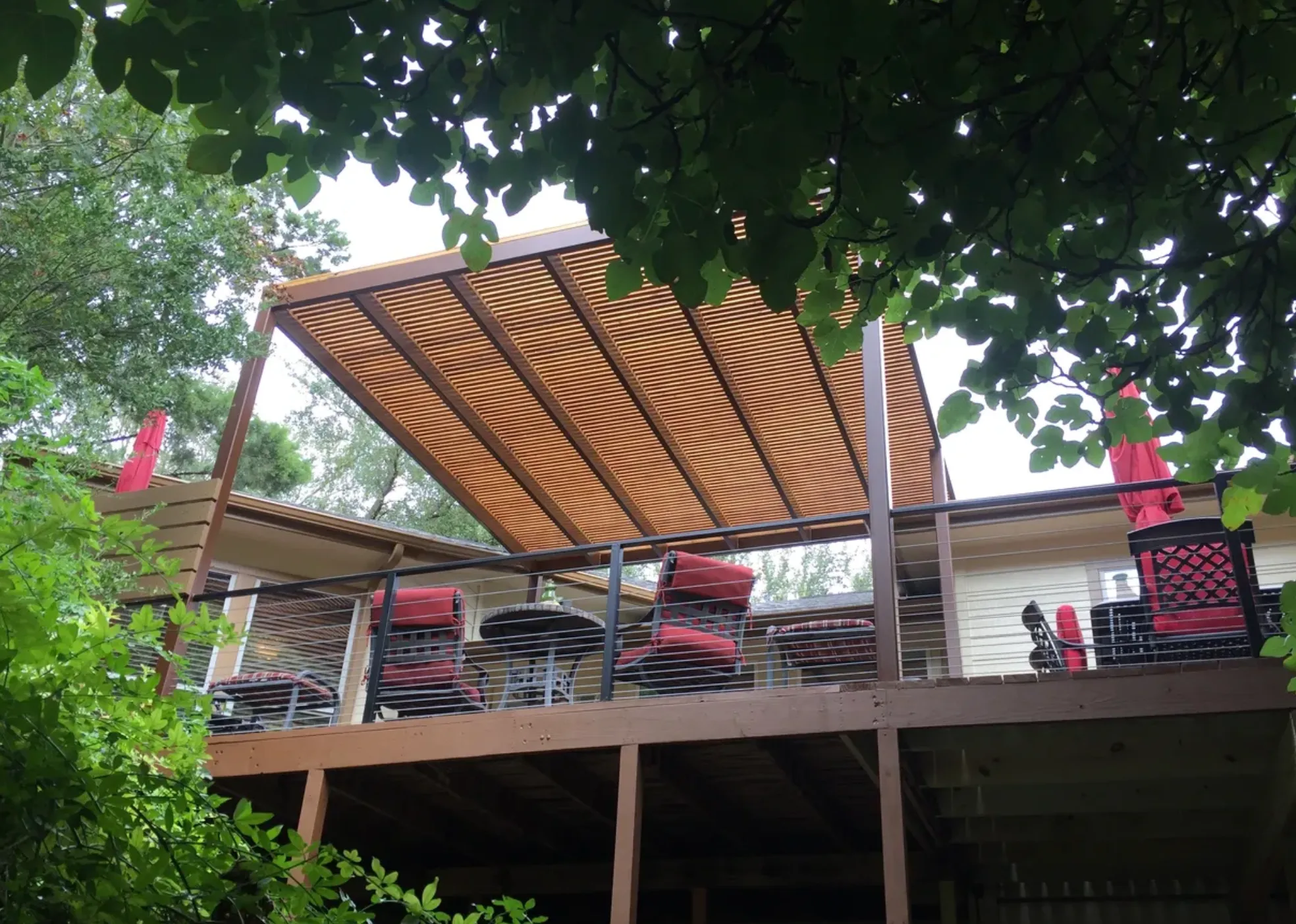 Steel-framed pergola with wood slats over an outdoor deck with red chairs