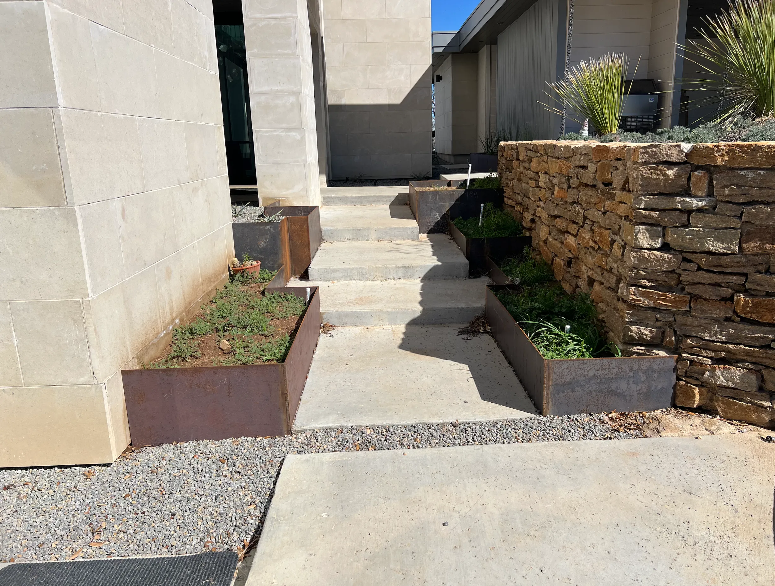 Steel planters lining a concrete walkway next to a stacked-stone wall