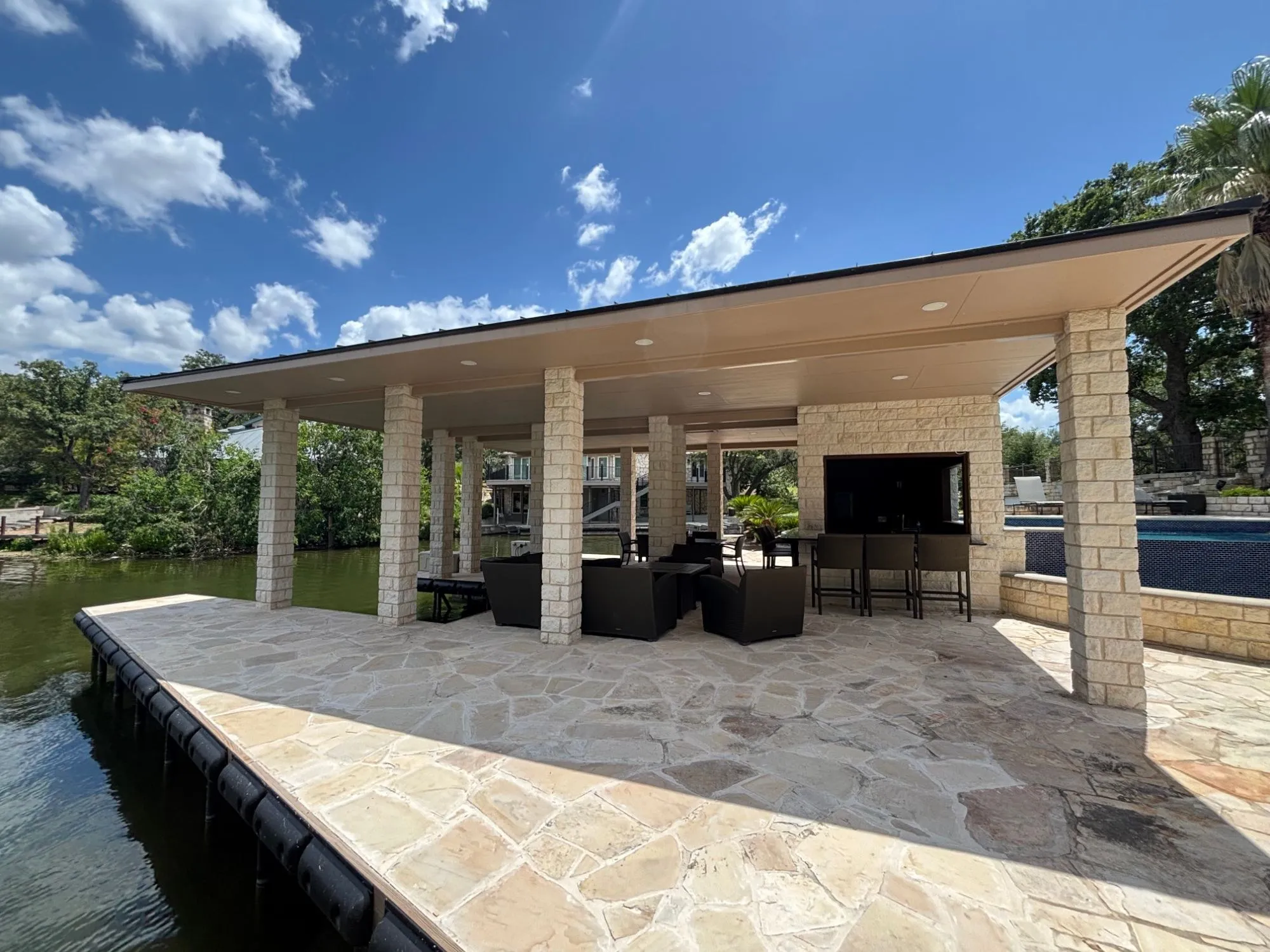 Stone pavilion dock with a flagstone deck and limestone columns under a wide roof, seen from the edge of the dock on the lake