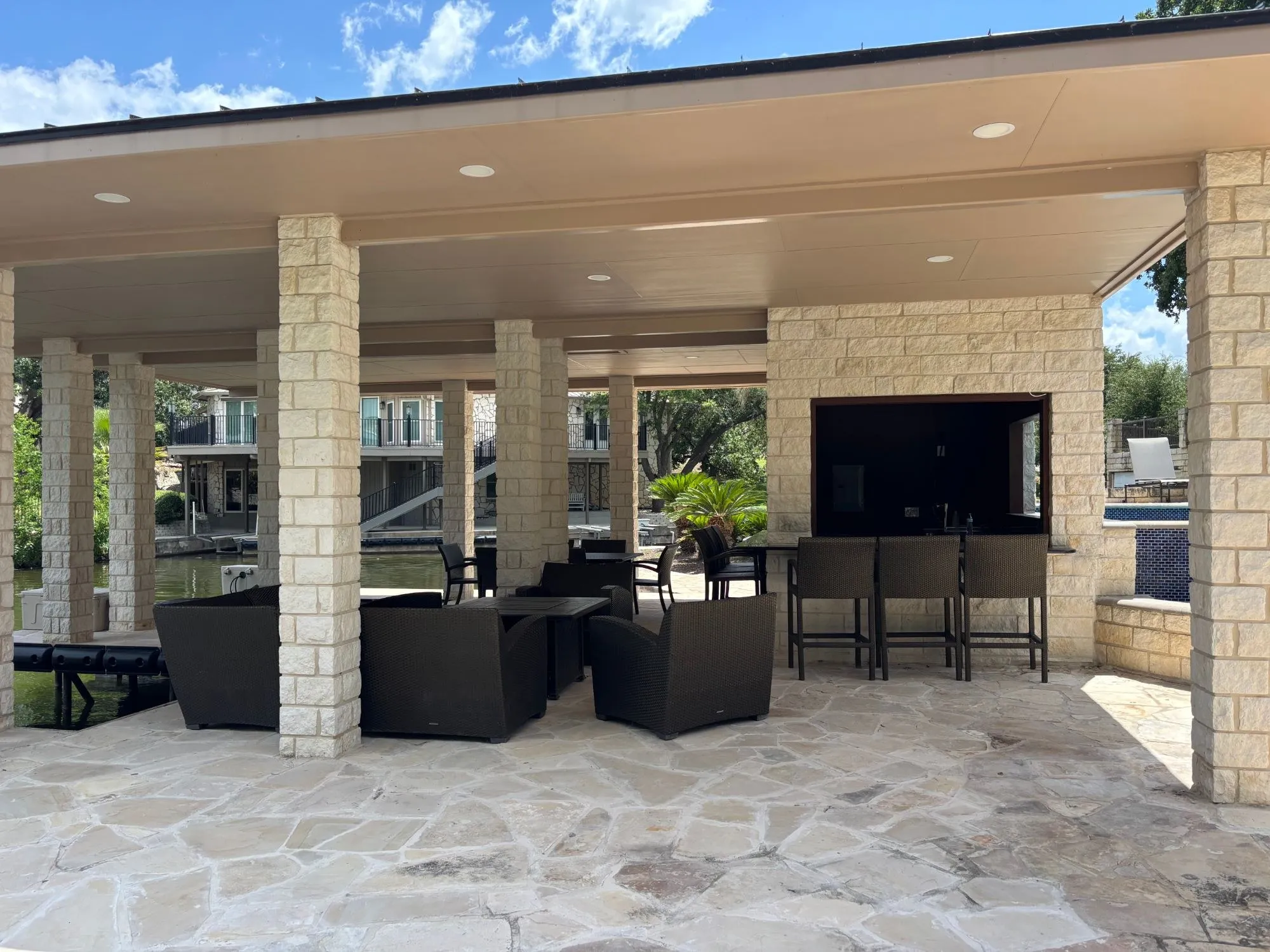 Front view of the pavilion dock with lounge seating, bar stools and limestone columns, with the lake and neighboring homes behind
