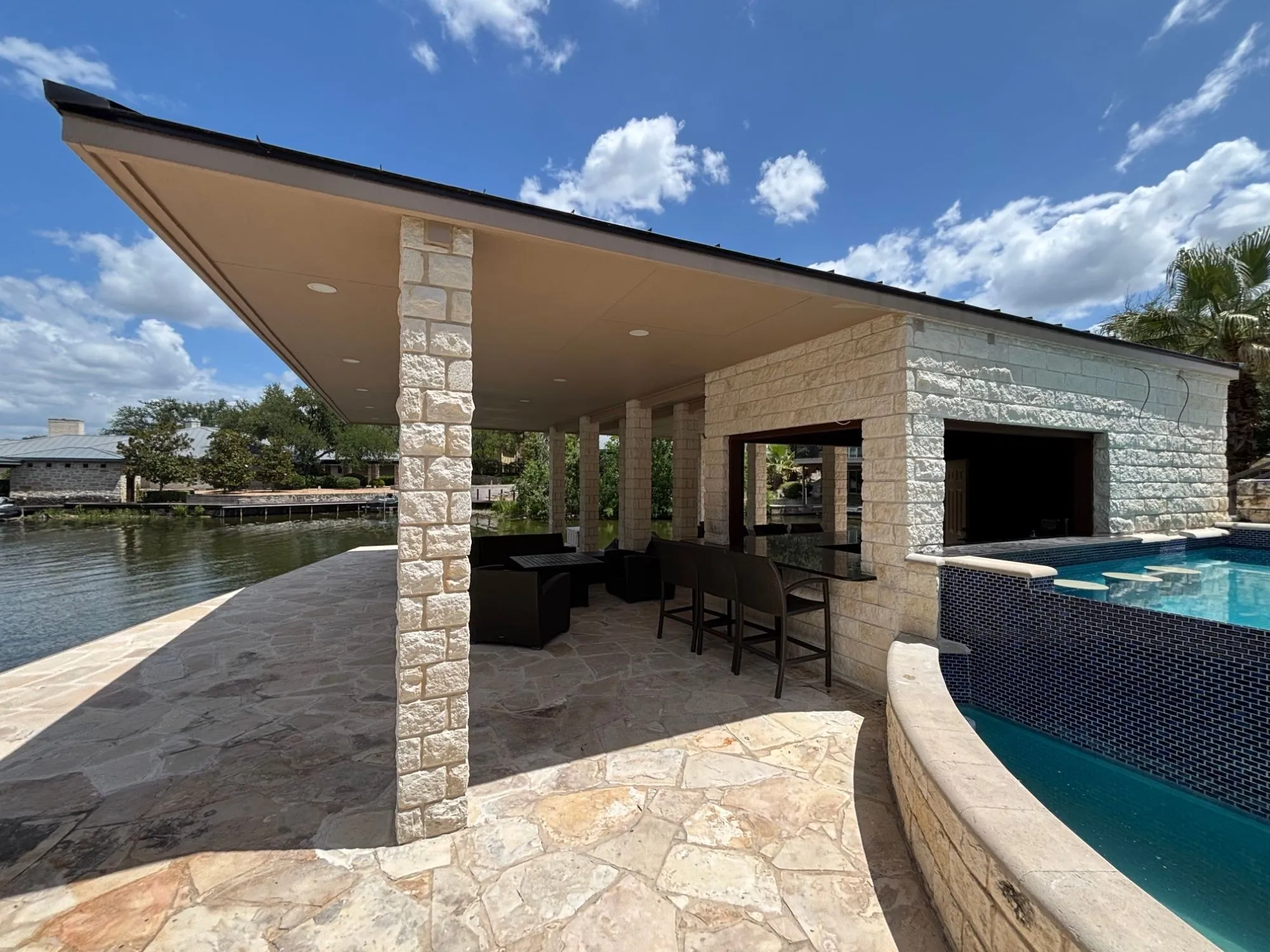 The pavilion and its outdoor bar from the pool side, with the bar window opening toward the pool and the lake beyond